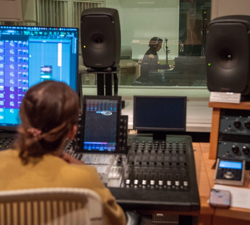 A student sitting behind a control booth managing a recording session